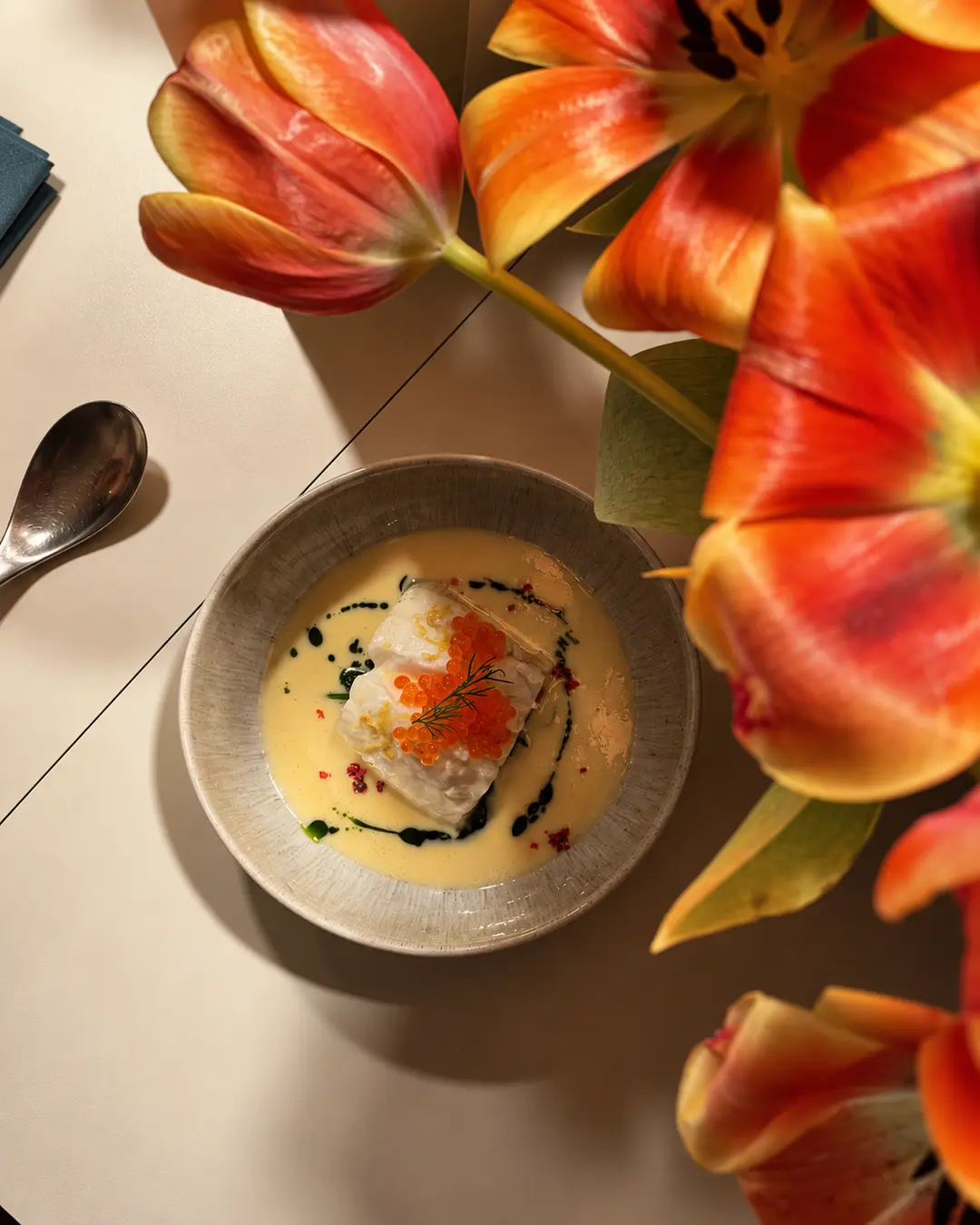 Fischgericht mit Kaviar in heller Sauce, umrahmt von orangefarbenen Tulpen