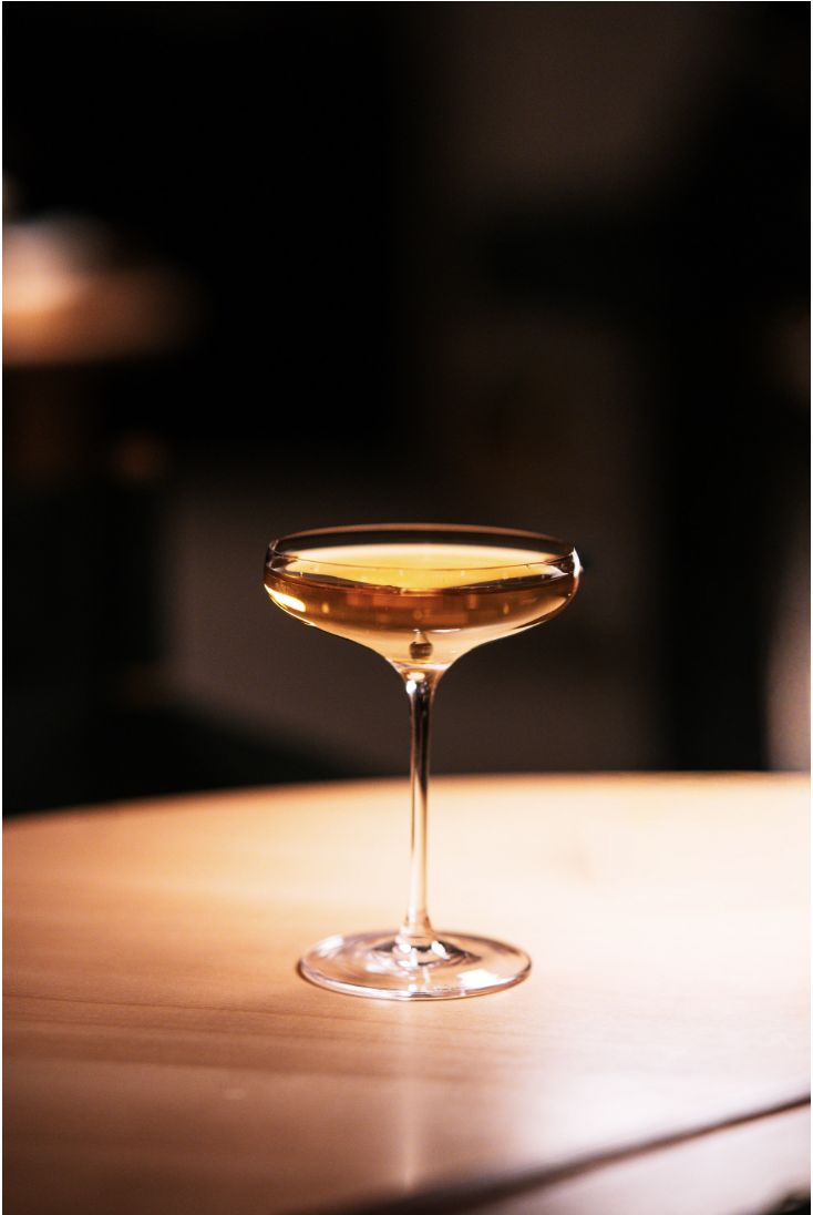 Goldener Cocktail im filigranen Stielglas auf einem warm beleuchteten Tisch